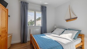 Ein Schlafzimmer mit Bett, einem Holzschrank, einem Fenster mit Vorhängen und einer Segelboot-Dekoration.