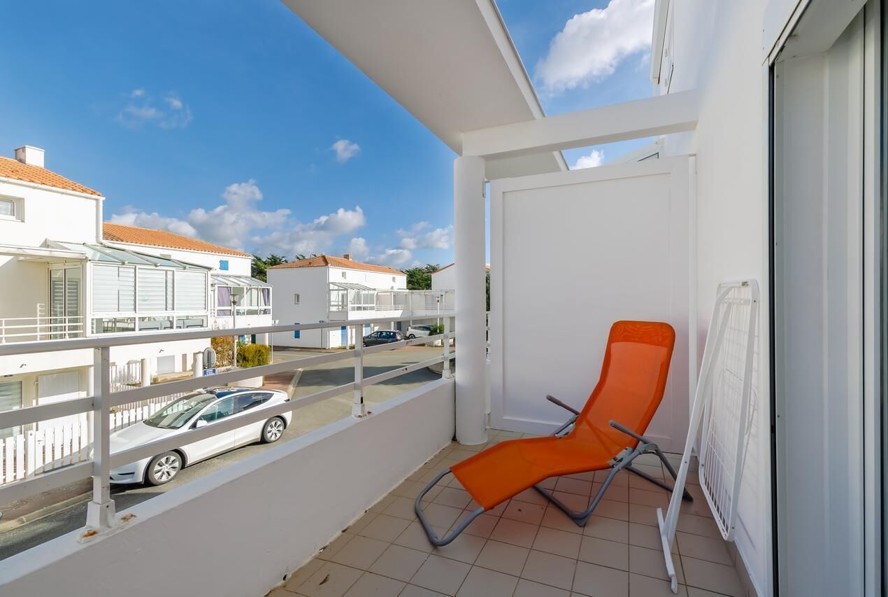 Ein Balkon mit weißem Geländer, einer weißen Tür und einem orangefarbenen Stuhl.
