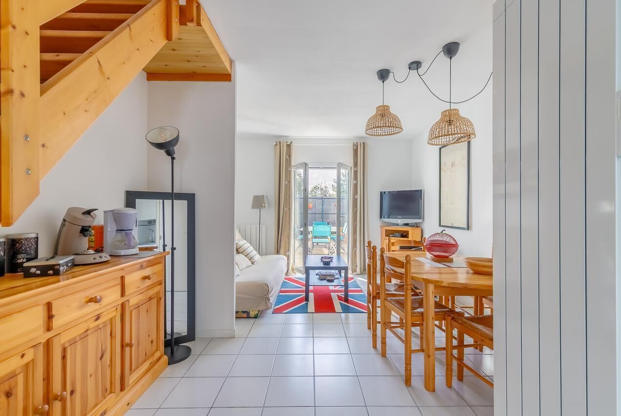 A modern kitchen with wooden cabinets, a coffee machine, and a dining area with wooden chairs and a table.