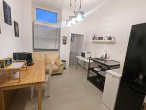 Cozy living space with a dining area, sofa, and bench, featuring a television and kitchenette with a refrigerator, sink, and microwave.