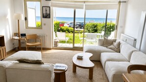 A living room with a sofa, a coffee table, a chair, a lamp, and a view of the sea through large windows.