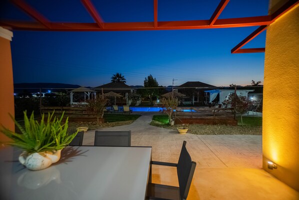 Un patio al aire libre con piscina, mobiliario y vistas del barrio circundante al anochecer.