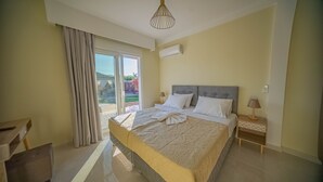 Une chambre moderne avec un grand lit, une table de chevet avec une lampe et une vue sur l’extérieur grâce à une porte-fenêtre coulissante.