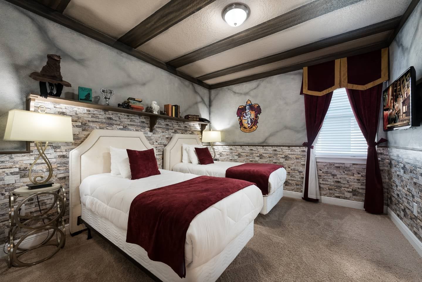 A hotel room with two beds, a stone wall, a ceiling with exposed beams, a fireplace, and a window with curtains.