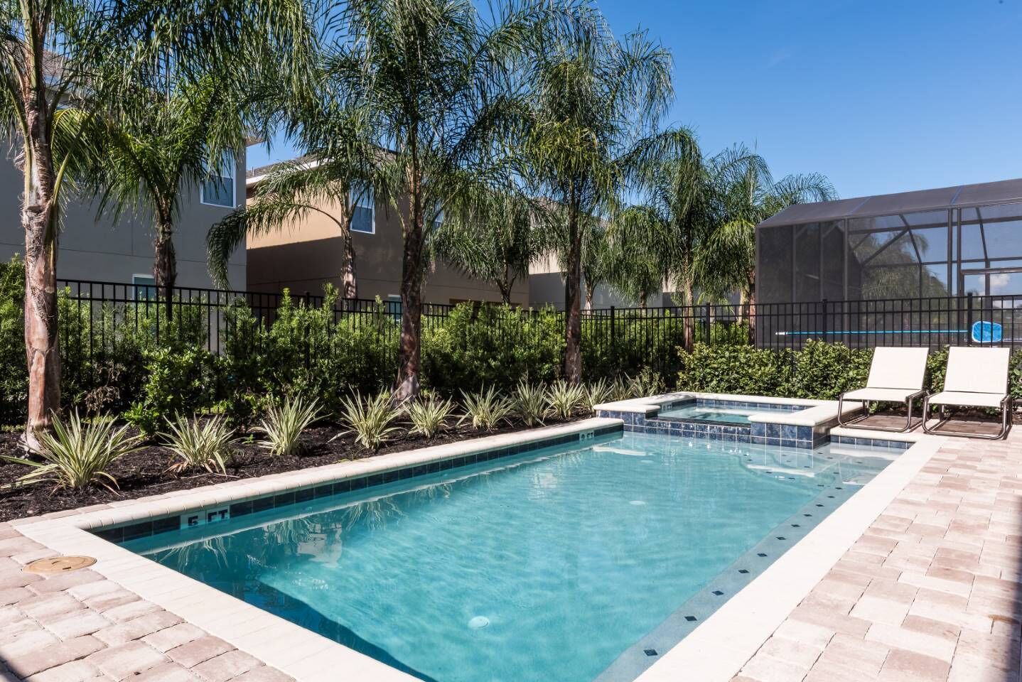 A rectangular pool with a tiled edge, surrounded by a brick patio. There are two lounge chairs and a small hot tub area.