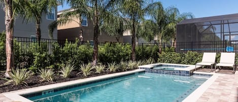 Una piscina rectangular con borde de azulejos, rodeada por un patio de ladrillo. Se observan dos sillas de descanso y una pequeña zona de hidromasaje.