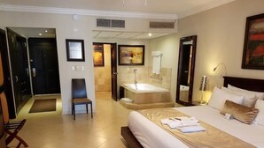 A hotel room with a large bed, a bathroom with a bathtub, and a seating area with a bench.