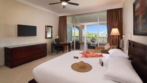 A hotel room with a bed, a desk, a dresser, a ceiling fan, and a large window with curtains.