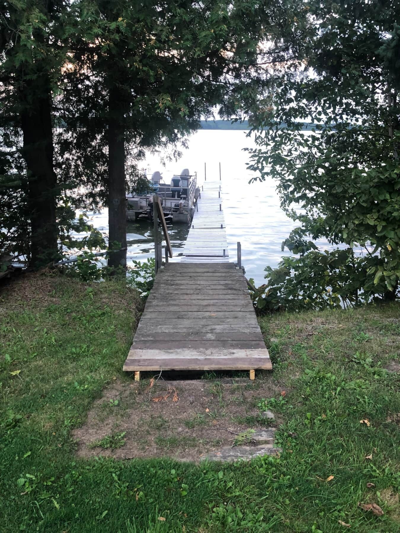 A wooden dock leading to a boat docked on calm water, surrounded by trees.
