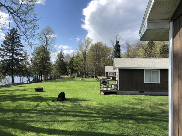 A grassy yard with a wooden cabin, a barbecue grill, and a picnic table.