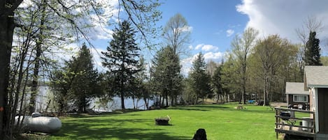 A grassy area with a wooden deck and a building, likely a cabin or lodge, near a body of water.