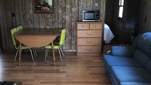 Un espacio habitable compacto con piso de madera, una mesa de comedor con sillas, un sofá azul, un pequeño aparador y un televisor.