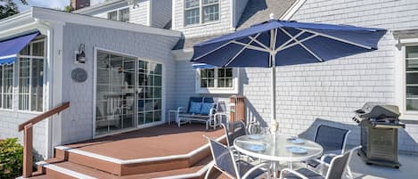 Ein Haus mit einer Terrasse, inklusive Tisch und Stühlen, einem Grill und einem überdachten Bereich mit einem blauen Sonnenschirm.