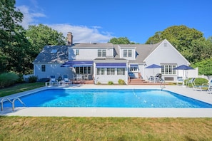 Uma casa de dois andares com piscina, área de estar ao ar livre e varanda coberta.