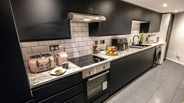 Eine moderne Küche mit dunklen Schränken, einer Edelstahl-Dunstabzugshaube, einer eingebauten Mikrowelle und einer Arbeitsplatte mit Obstschale und Toaster.