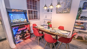 Ein Essbereich mit einem Retro-Arcade-Spiel, roten Stühlen, einem Holztisch und einem Bücherregal mit Büchern und einem Stofftier.