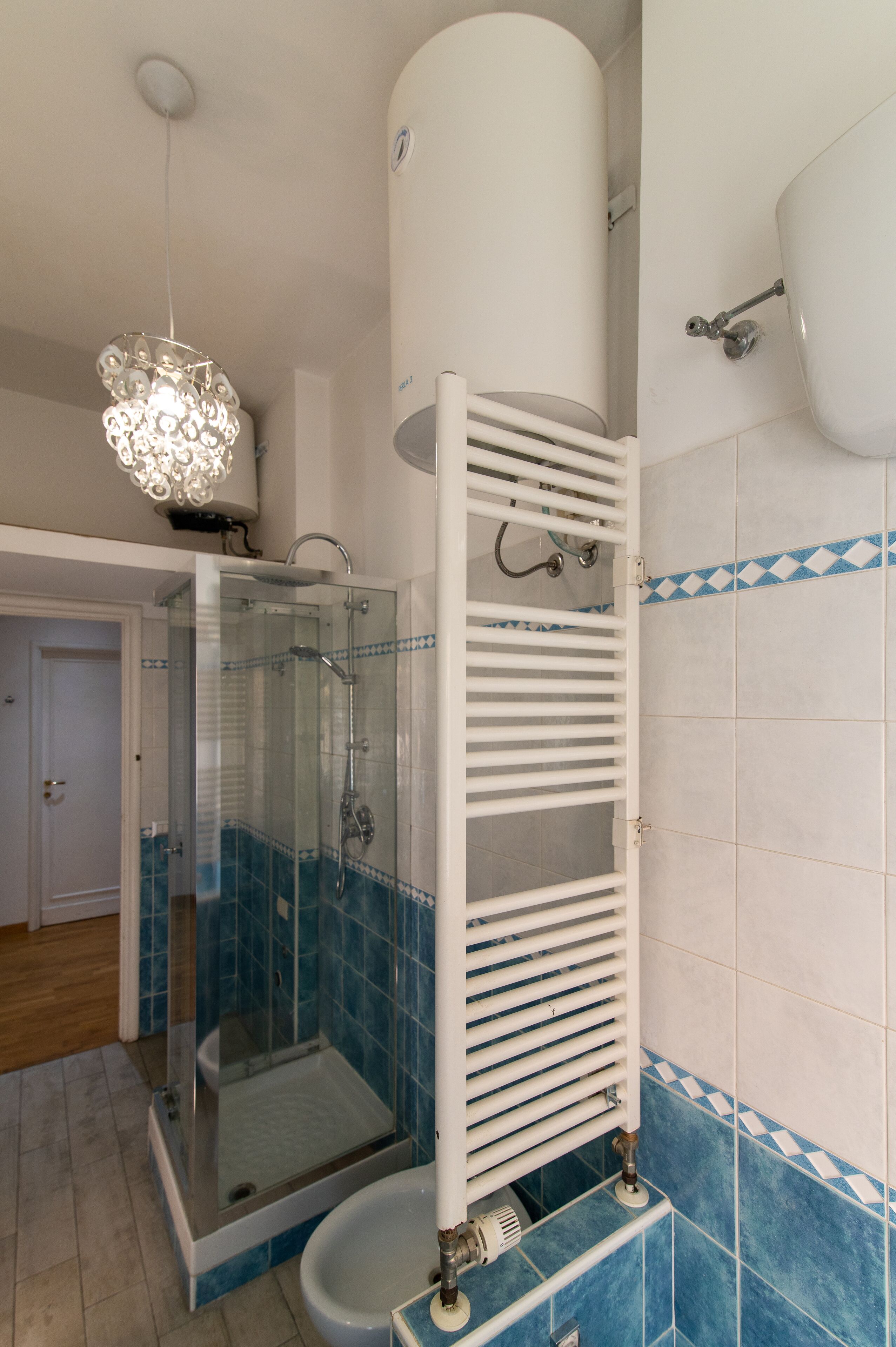 A bathroom with a glass-enclosed shower, a white towel rack, and blue-tiled walls.