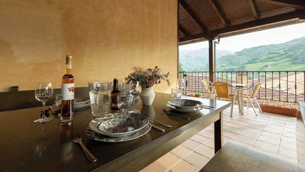 Une table à manger dressée avec des assiettes, des couverts et des verres, donnant sur un paysage pittoresque.