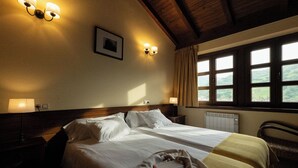 Une chambre d’hôtel avec un grand lit, deux lampes de chevet, une fenêtre avec des rideaux et une vue sur la verdure.
