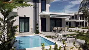 Una casa moderna de dos pisos con piscina, mobiliario exterior y un jardín bien cuidado.