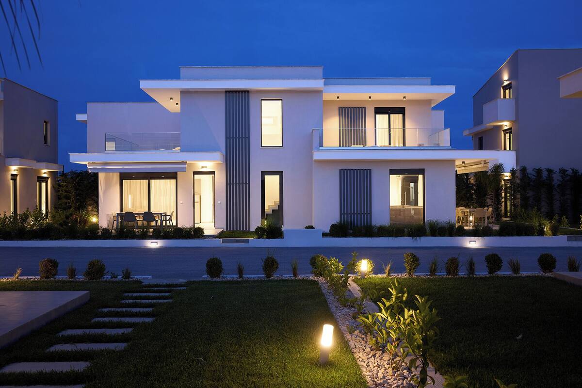 A modern two-story house with a flat roof, large windows, and a well-lit outdoor patio.