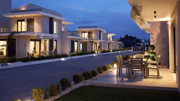 Una zona residencial moderna con casas contemporáneas, una calle pavimentada y mobiliario exterior.