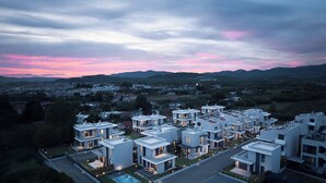Un moderno complejo residencial con varias edificaciones blancas, una piscina y vistas a colinas distantes.