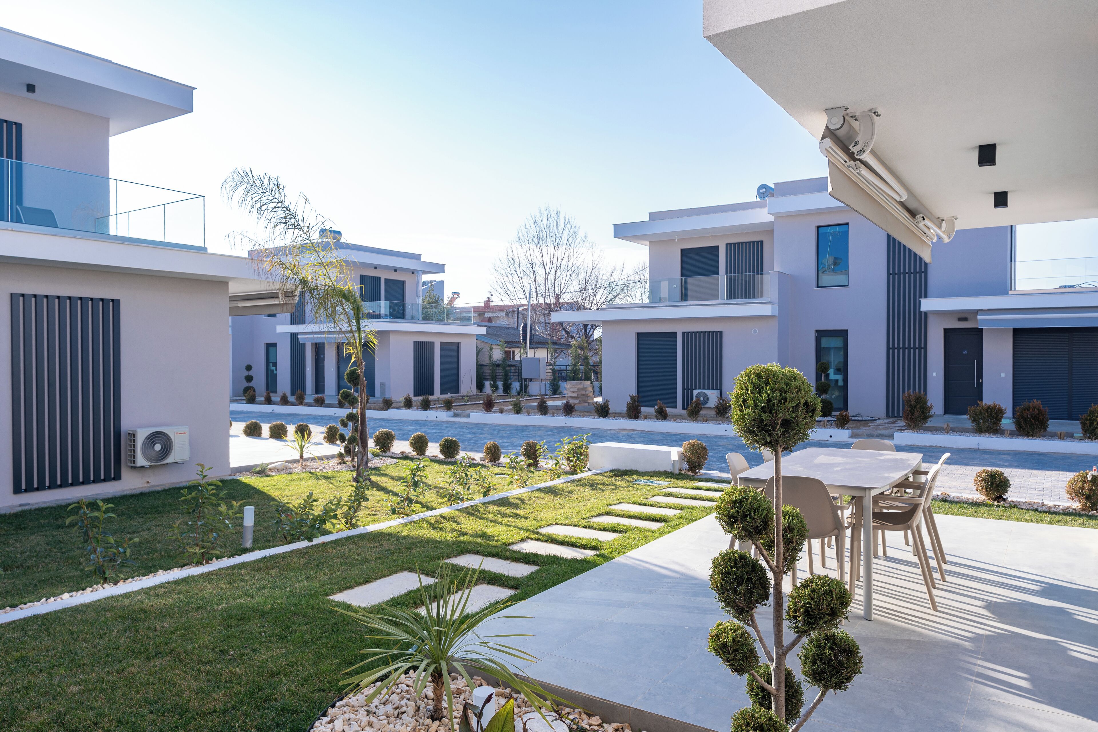 A modern residential complex with multiple buildings, a well-maintained lawn, and a patio area with outdoor furniture.