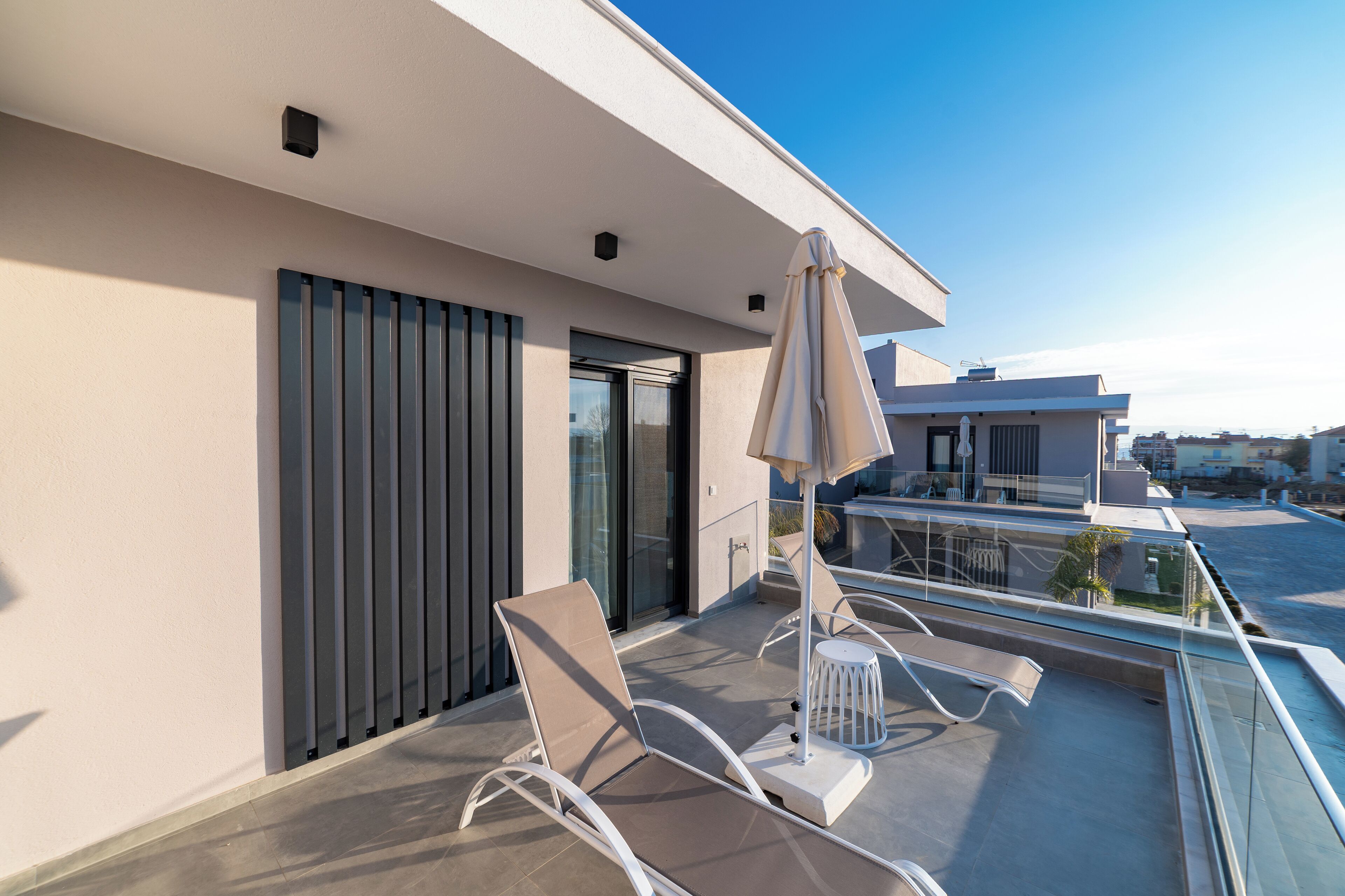 A balcony with two lounge chairs, a table, and an umbrella.