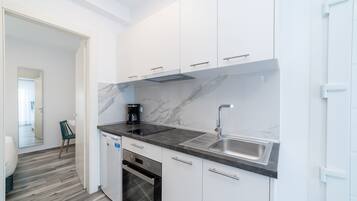 Uma cozinha moderna com armários brancos, painel de fundo de mármore, forno embutido e pia de aço inoxidável.