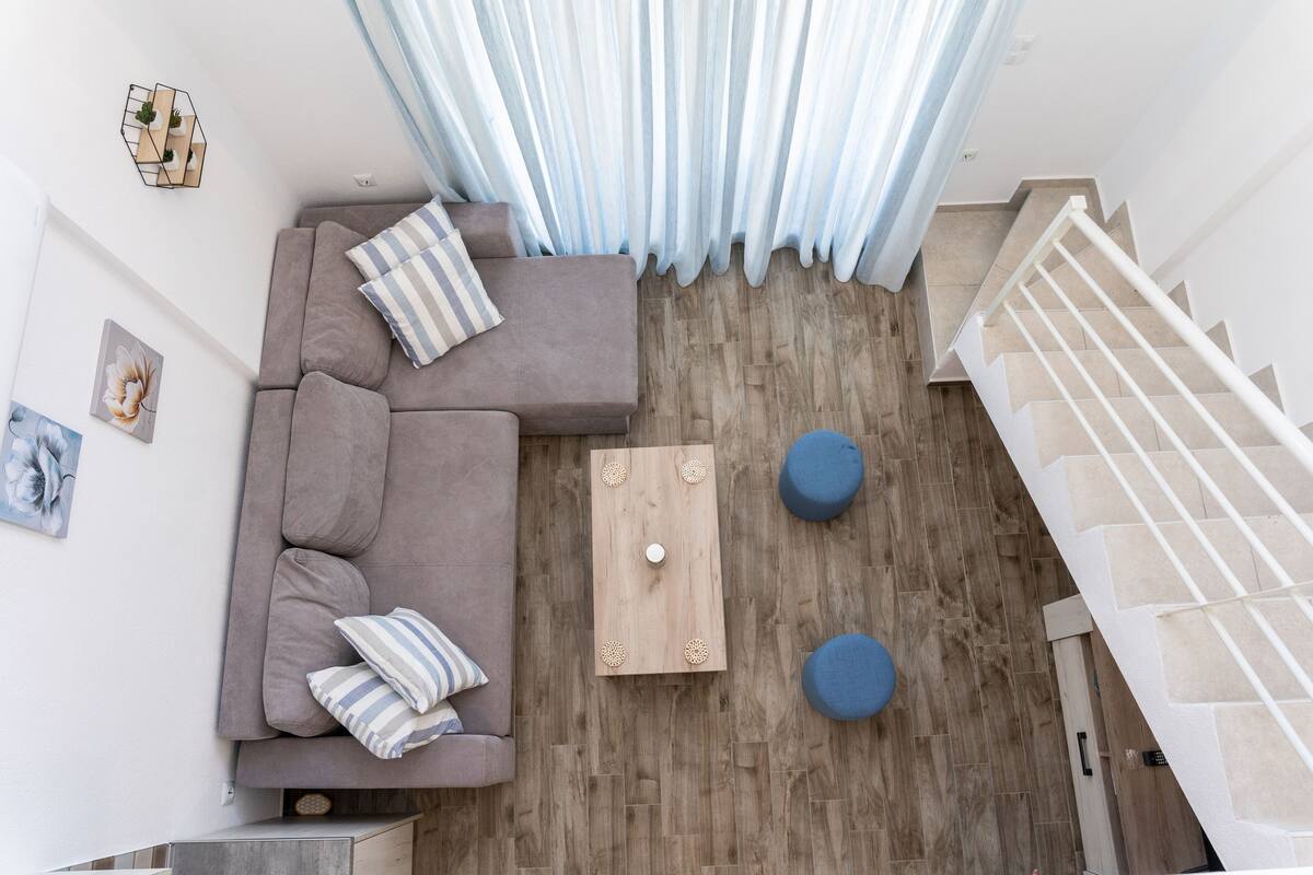 A modern living room with a grey sectional sofa, a wooden coffee table, and two blue ottomans.