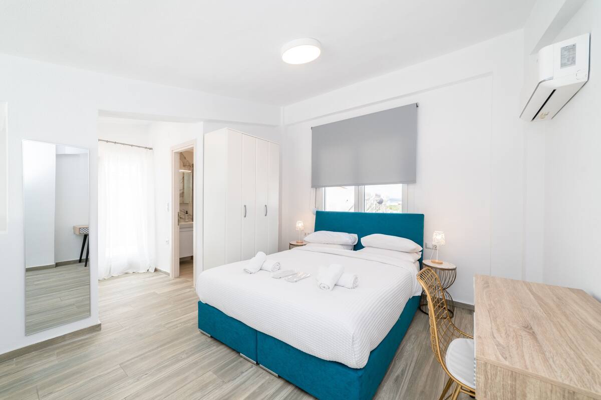 A modern hotel room with a large bed, a desk, and a wardrobe.