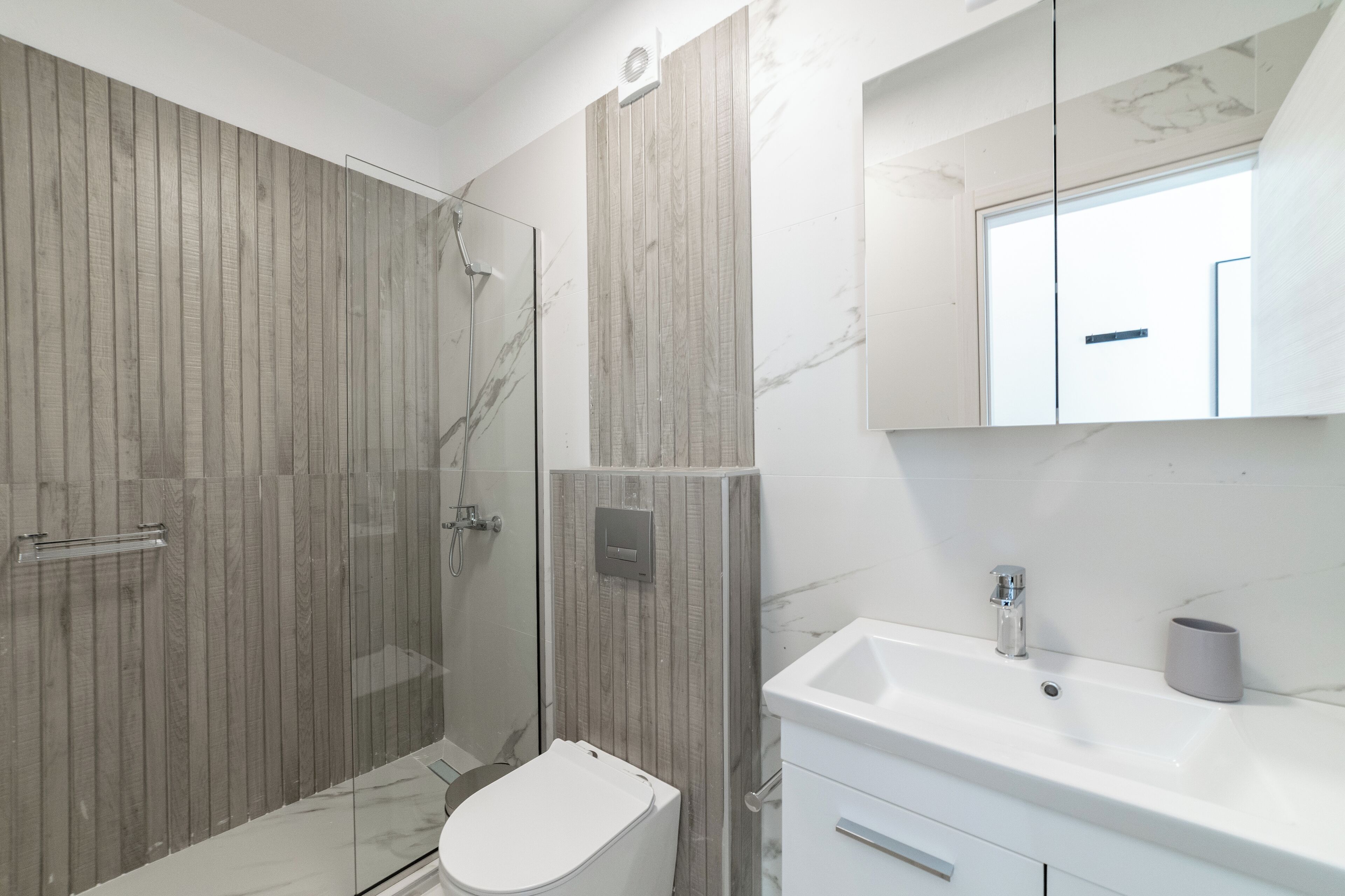 Een moderne badkamer met een douchecabine van glas, een wit toilet en een marmeren wastafel met een wastafel en spiegel.