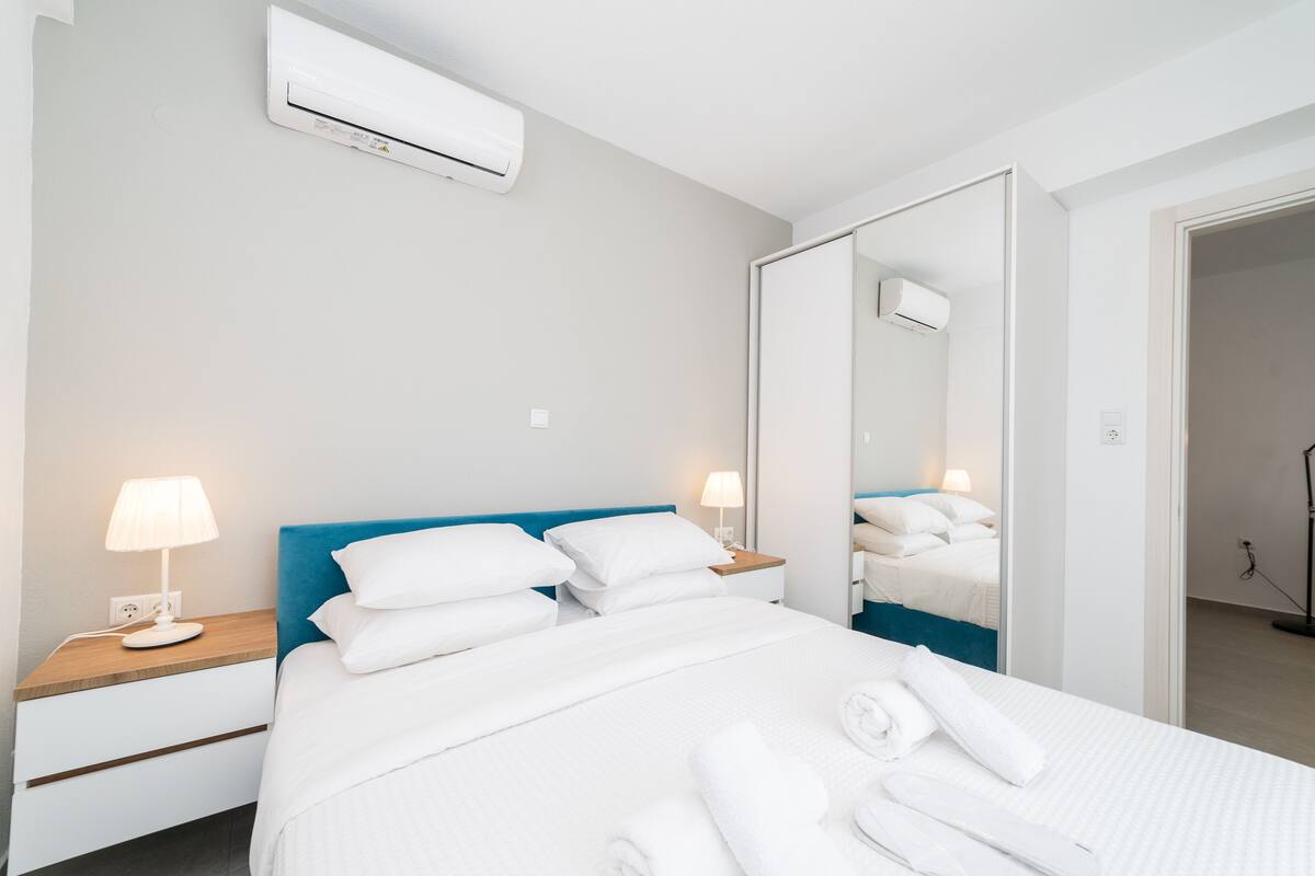 A hotel room with a bed, bedside lamps, a mirror, and an air conditioning unit.