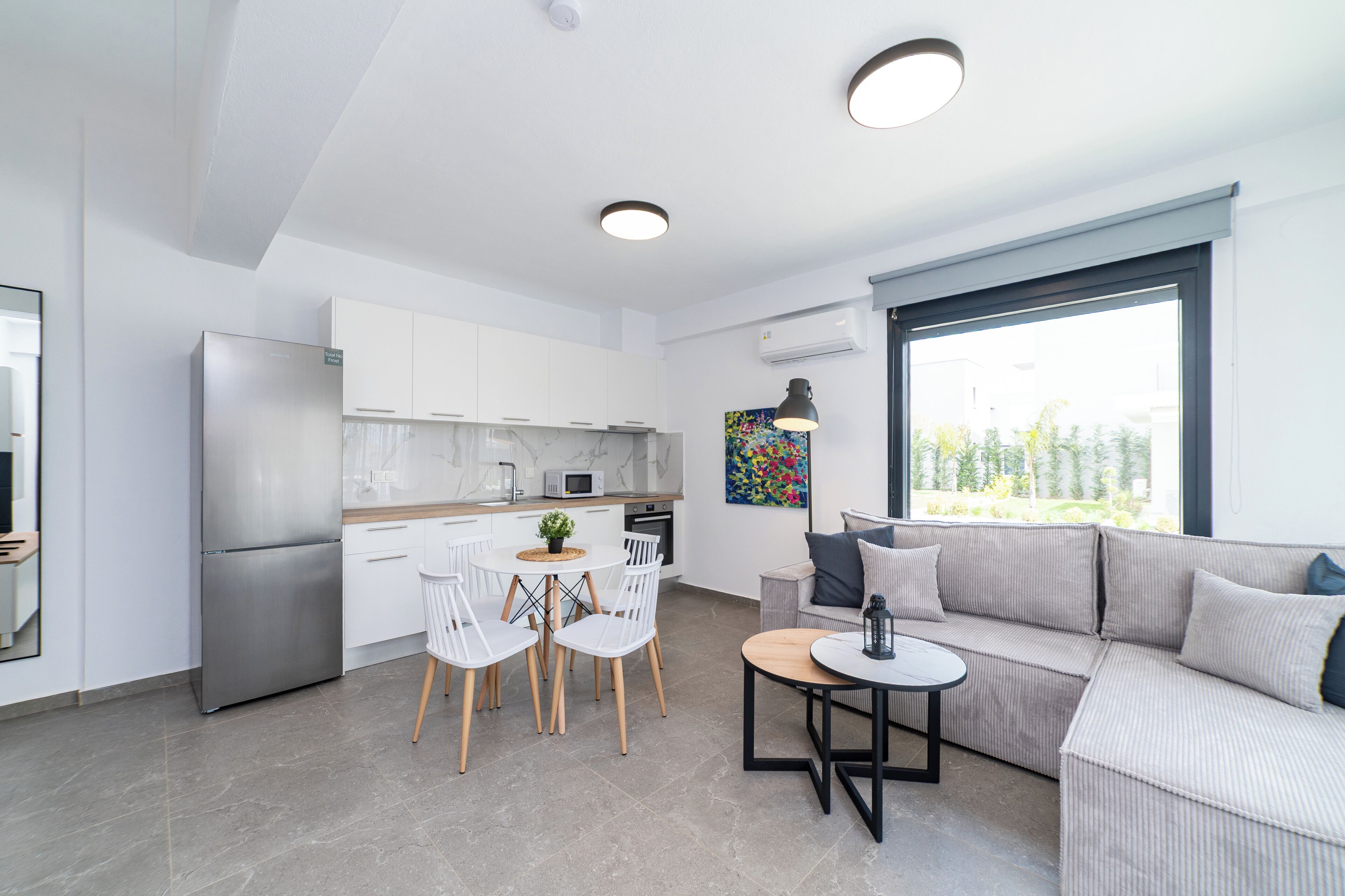 Een moderne keuken met witte kastjes, een roestvrijstalen koelkast en een eethoek met een ronde tafel en stoelen.