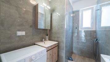 A modern bathroom with a washing machine, a sink, and a shower area.