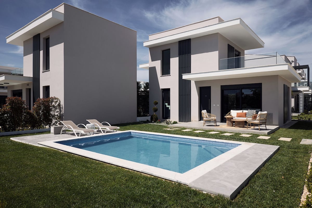 A modern two-story house with a swimming pool, outdoor seating, and a well-maintained lawn.