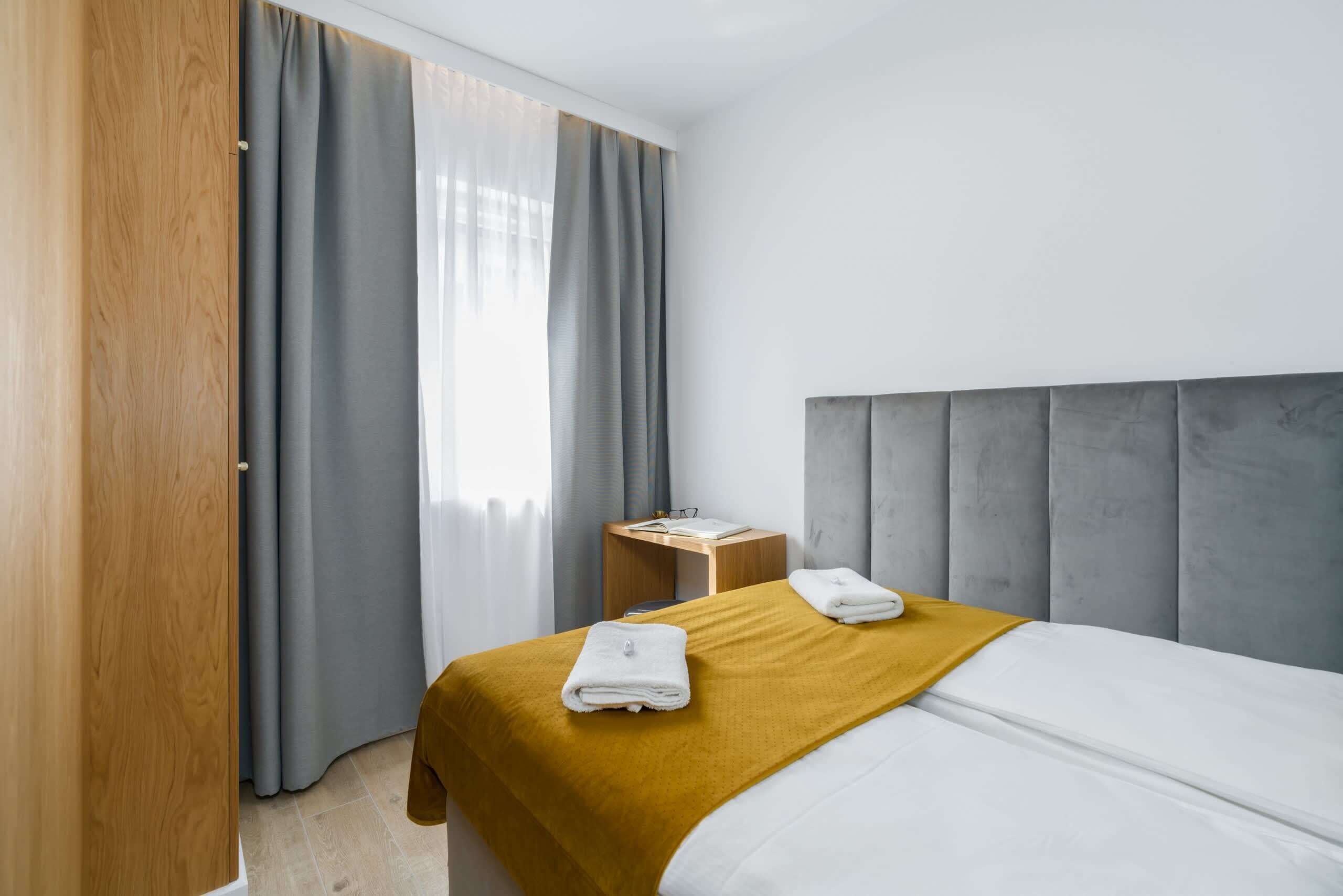 A hotel room with a bed, a wooden wardrobe, a nightstand, and a window with curtains.