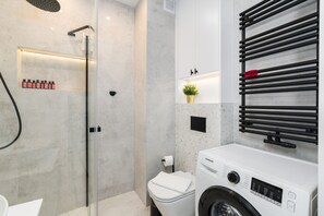 A modern bathroom with a glass-enclosed shower, a white toilet, a washing machine, and a towel rack.