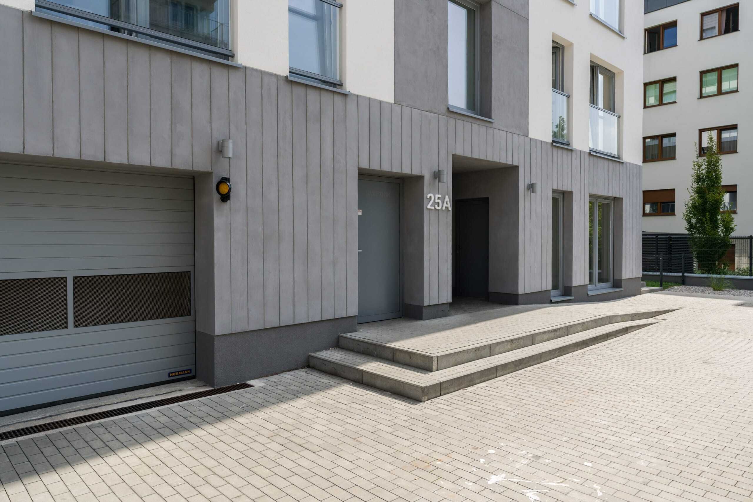 Un edificio moderno con fachada gris, una puerta de garaje y un cartel con el número 25A.