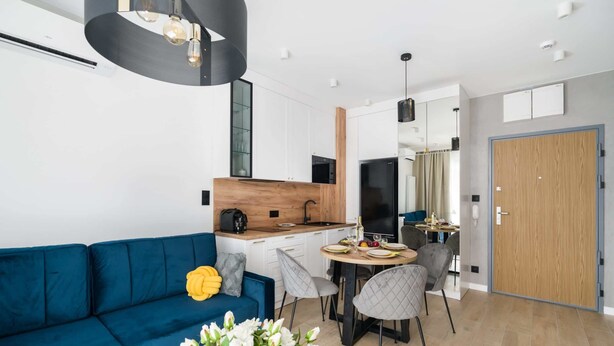 Un salon moderne avec un canapé bleu, une table à manger avec des chaises et un coin cuisine doté d’un plan de travail en bois et d’appareils électroménagers.