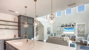 A spacious kitchen with a large island, pendant lighting, and a view to the living area. - Luxe Island Escape by Beach Boutique Rentals (Anna Maria)