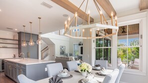 A spacious dining area with a long table, elegant lighting, and a view of greenery through large windows. - Luxe Island Escape by Beach Boutique Rentals (Anna Maria)