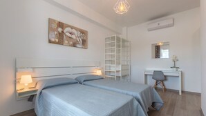 A bedroom with two beds, a desk, a chair, a bookshelf, and a hanging light fixture.