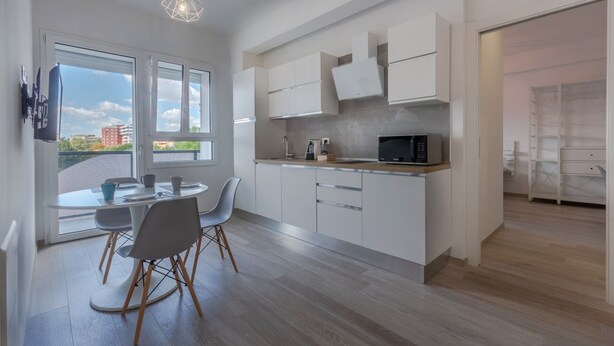 A modern kitchen with white cabinets, a microwave, and a dining area with a table and chairs.