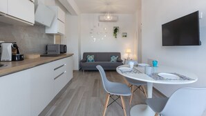 A modern kitchen with a dining area, a sofa, and a TV mounted on the wall.