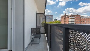 A balcony with a table and chairs, a metal fence, and a view of buildings in the background.