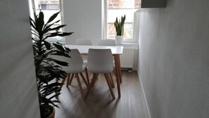 A dining area with a white table and chairs, a potted plant, and a window with a view of buildings.