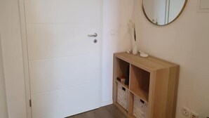 A white door with a silver handle, a wooden console table with a mirror above it, and a small vase with flowers.