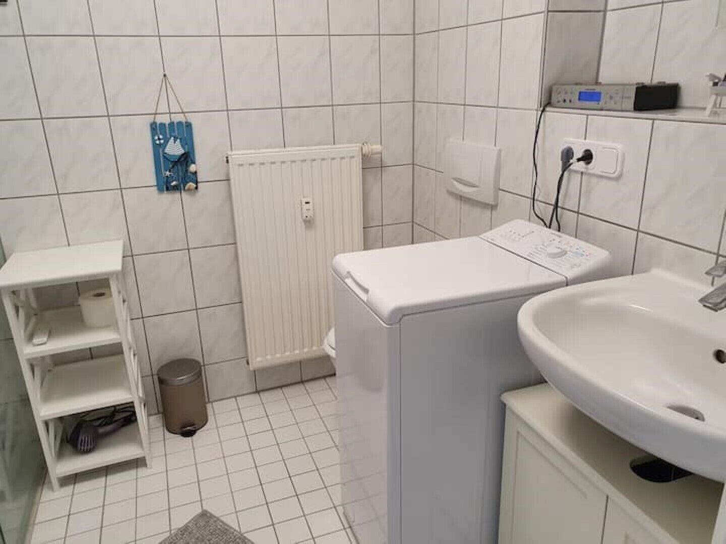 A small, clean bathroom with a white sink, a washing machine, and a shelf with toiletries.